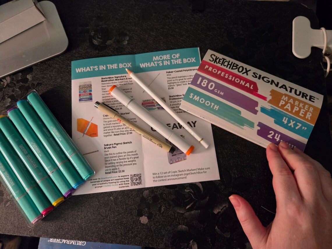 August SketchBox unboxing featuring professional alcohol markers, Copic Sketch marker, Sakura Pigma Brush Pen, Faber-Castell Polychromos pencil, and SketchBox Signature marker paper before creating the monthly project.