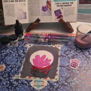 September 2026 SketchBox crystal ball mixed-media painting with pink and purple crystals, a dark background, and red and black base surrounded by the project supplies.
